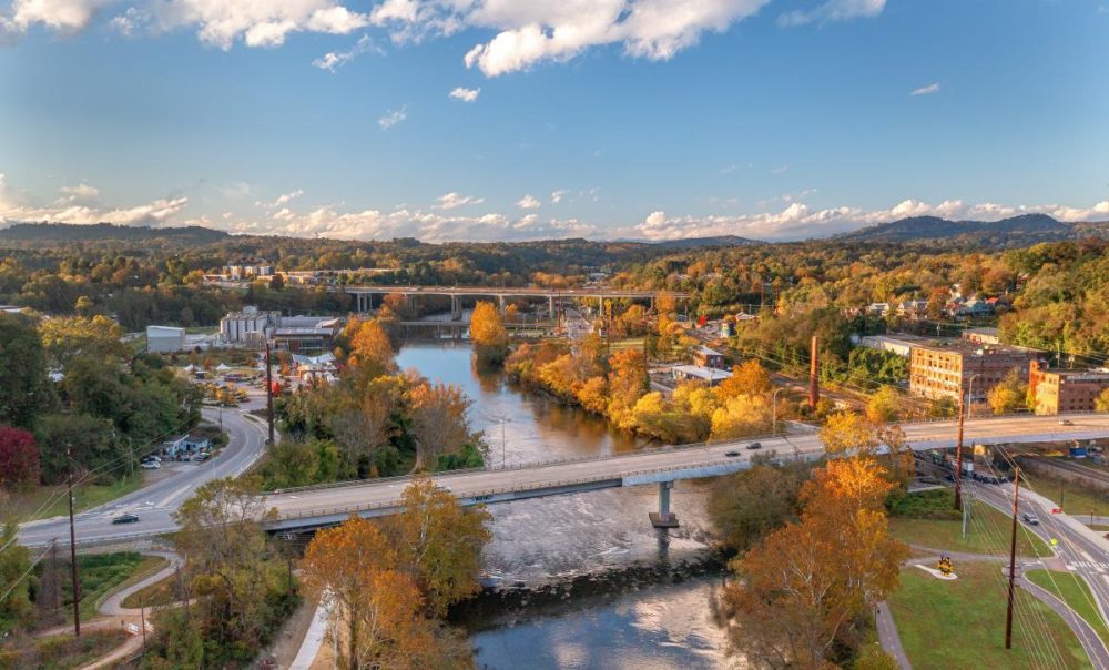 Aerial view of a river with bridges and autumn trees around, under a partly cloudy sky.