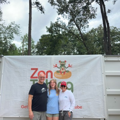 Three people smiling in front of a Zen Frog banner outdoors.