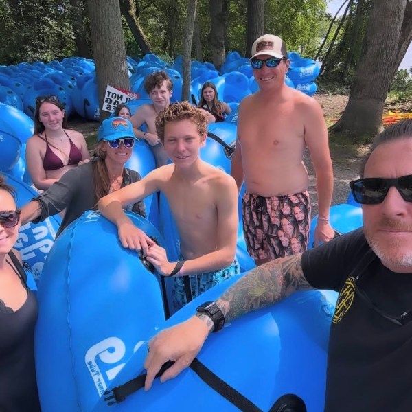 Group of people with blue inner tubes in a wooded area, enjoying a sunny day outdoors.