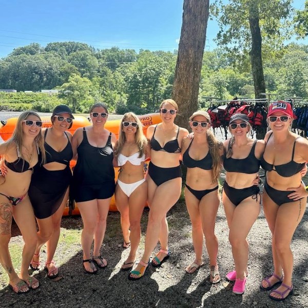 Bachelorette party group in swimsuits and sunglasses posing by stacked tubes outdoors.